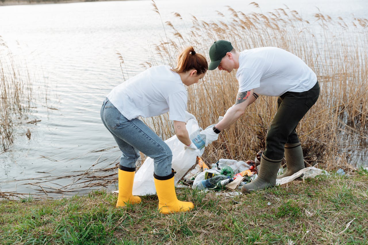 gallery-1 Two volunteers pick up trash by a river, promoting environmental conservation.